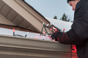 A man hangs Christmas lights while on a ladder