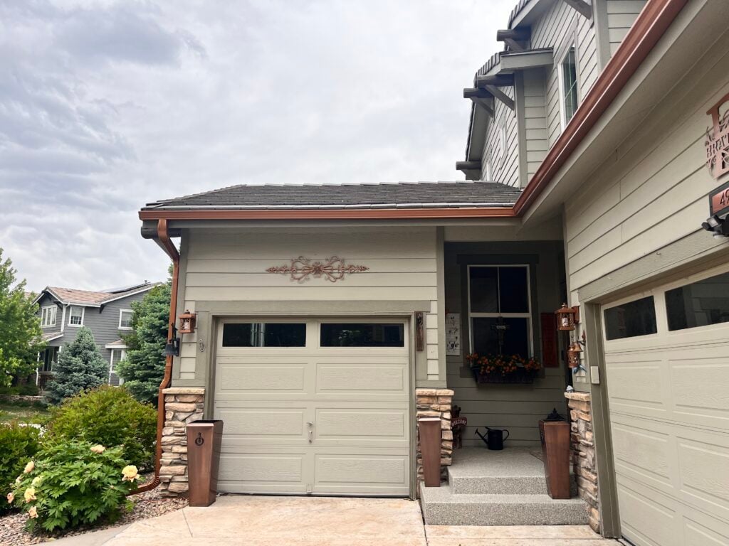 Copper Penny Open Gutters and downspouts. Gutters over garages in photo. copper accents and planters around a tan home.