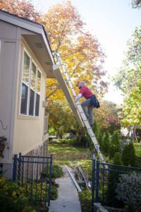 A picture of a man climbing a ladder to perform gutter maintenance