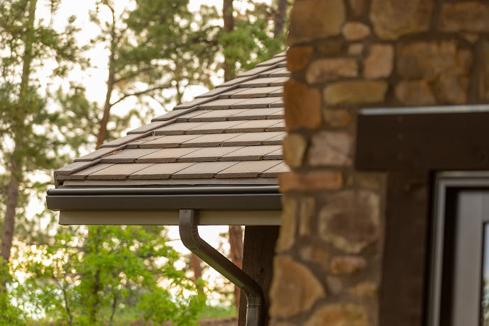 K-Guard hooded gutter and downspout along the eave of a stone-and-timber Colorado home surrounded by ponderosa pines