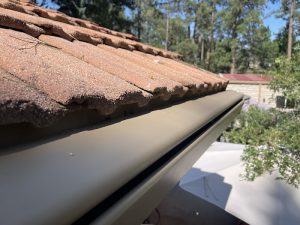 Cream K-Guard hooded gutter running along the edge of a tile roof on a Colorado home, with pines behind