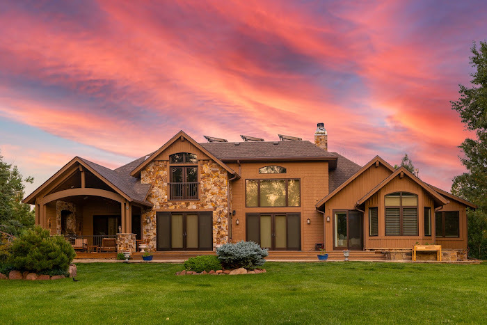 Rear elevation of a large stone-and-shake Colorado home at sunset with K-Guard gutters running along every roofline