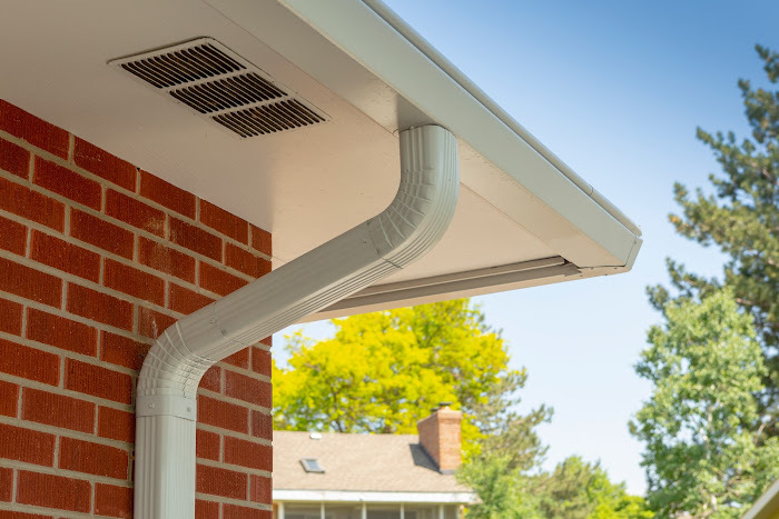 K-Guard downspout elbow carrying water down the corner of a red brick Colorado home beneath a hooded gutter