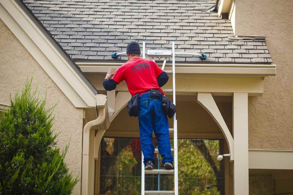 gutter company in Colorado Springs installing a new gutter system from a ladder
