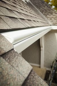 White covered gutters with a curved hood tucked along the shingle roof edge of a stucco Colorado home