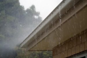 Water overflowing white gutter during rain storm. Clogged gutters. Clogged downspouts. Gutter failure. Can't handle water volume. Rain Overshooting gutter guard.