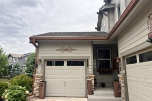 Copper Penny Open Gutters and downspouts. Gutters over garages in photo. copper accents and planters around a tan home.