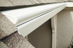 White covered gutters with a curved hood tucked along the shingle roof edge of a stucco Colorado home