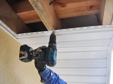 A technician uses a power drill to work on fascia boards